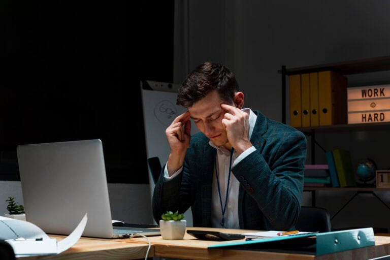Stressed professional man working late in office, rubbing temples, overwhelmed by work and deadlines