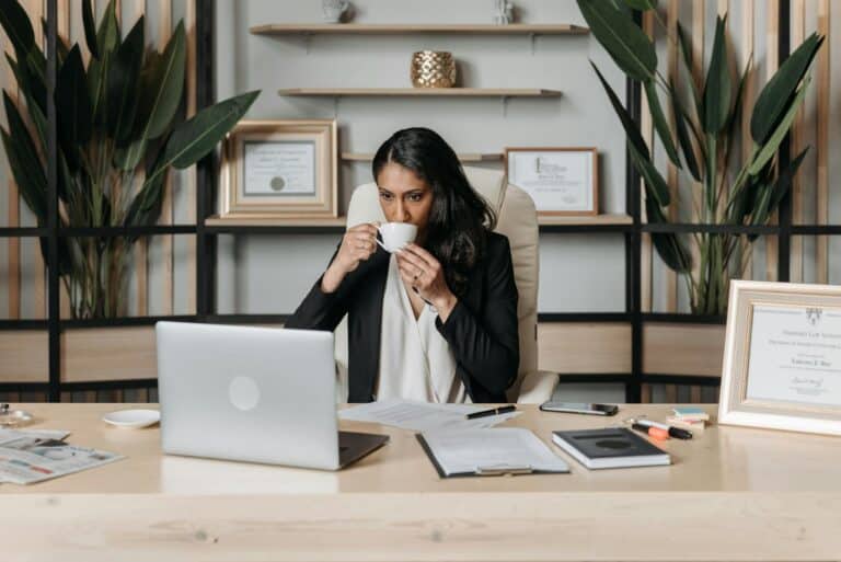 Fatigued midlife professional at desk with coffee cup, looking exhausted from work.