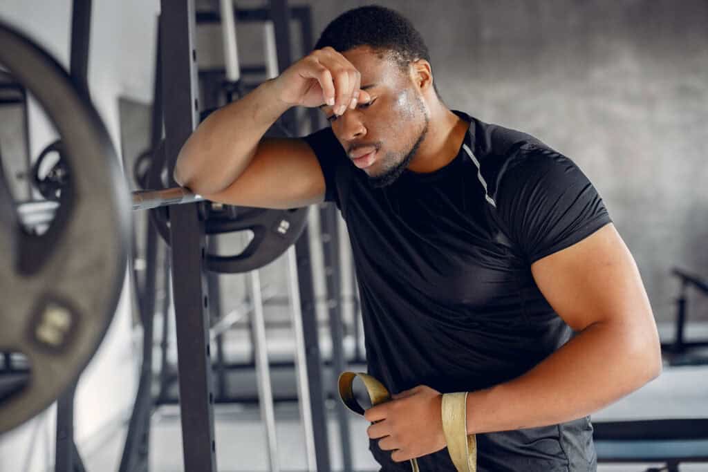 Mid-40s professional frustrated with fitness progress in home gym, leaning on weight bar—breaking the plateau after 40.