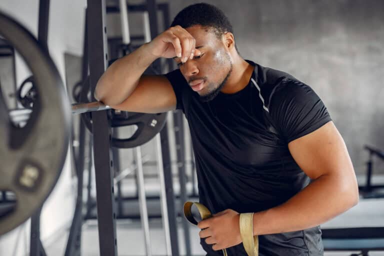 Mid-40s professional frustrated with fitness progress in home gym, leaning on weight bar.