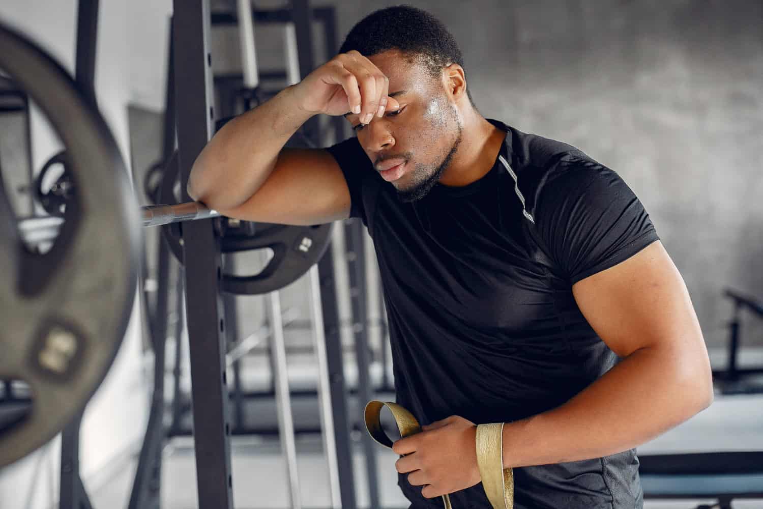 Mid-40s professional frustrated with fitness progress in home gym, leaning on weight bar.